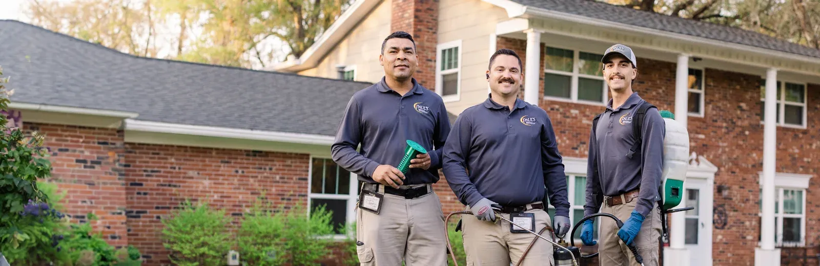 Paul's Pest Control Technicians standing in front of brick home